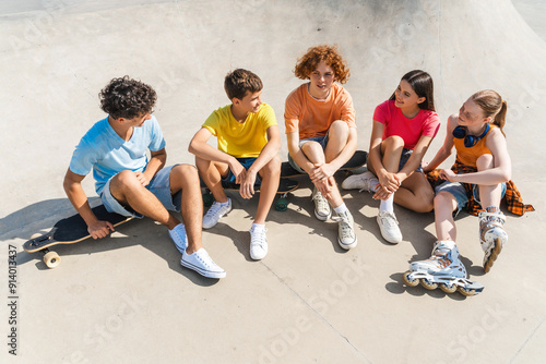 Group of smiling friends wearing colorful t shirts talking, sitting at the skate park photo