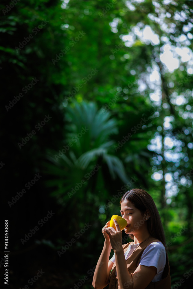 Fototapeta premium women enjoying her coffee during weekend during hiking activity in the rainy season, green big tree forest nature backgrounds.