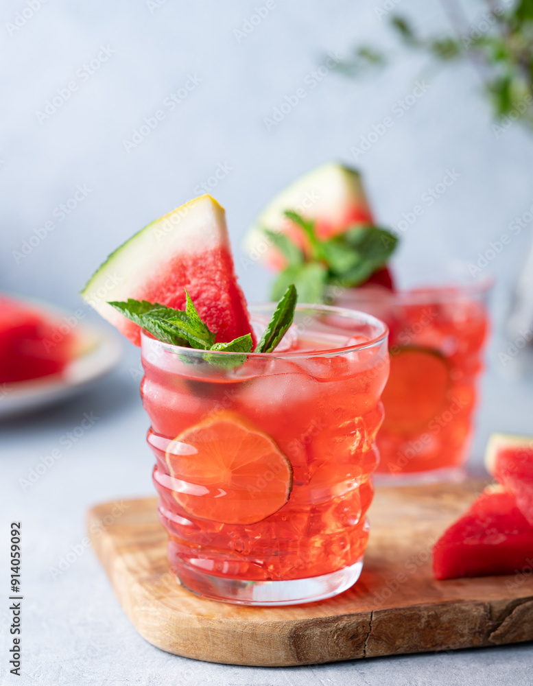 Two glasses watermelon cocktail with lime, ice and mint on a wooden board on a light background with branch and fruits close up. Two glasses watermelon cocktail with lime, ice and mint on a wooden board on a light background with branch and fruits close up.