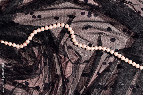 Elegant pearl necklace on black polka dot tulle fabric over pink background