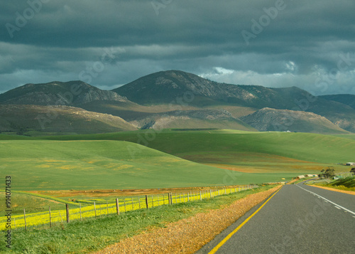 Open Road Leading to Green Hills Under Stormy Sky