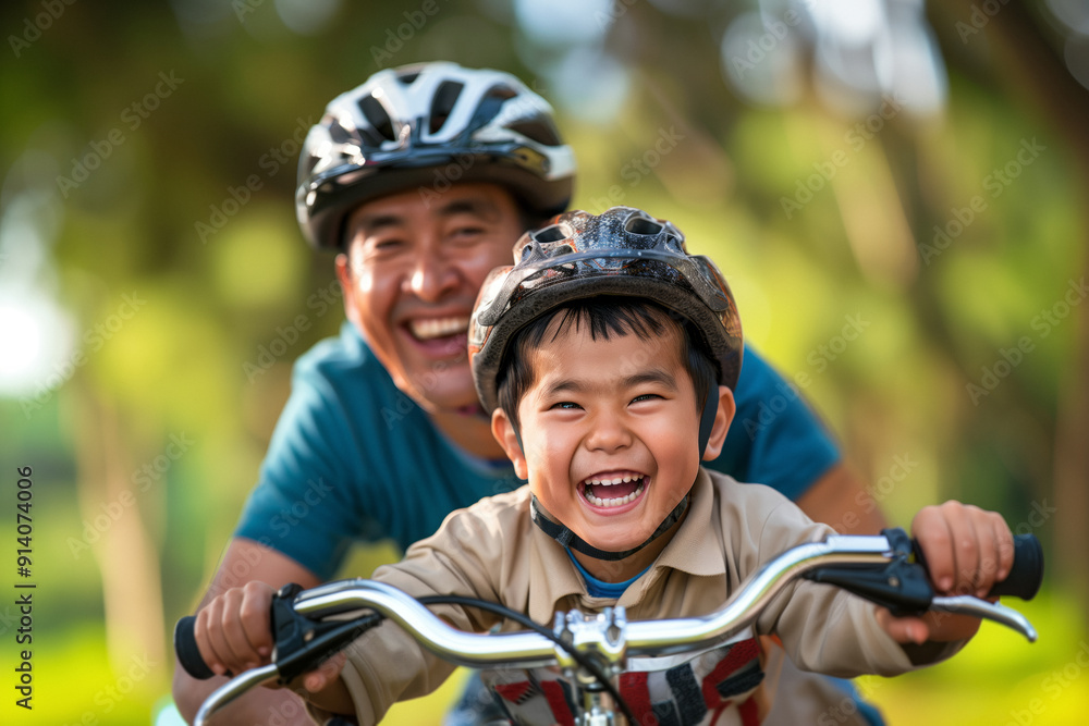Obraz premium Joyful Asian father and son riding bicycles in the park, both wearing helmets and smiling brightly. A moment of bonding and happiness in a natural outdoor setting.