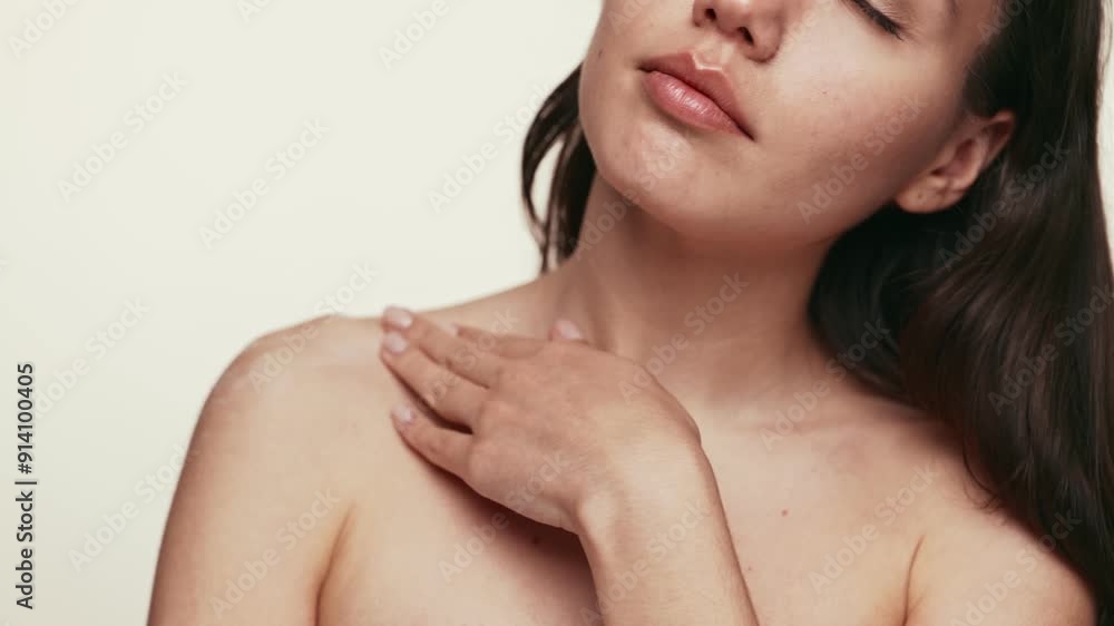 Close-up of a serene woman gently applying cream on her shoulder and neck, implying skincare and self-care. Close-up of a serene woman gently applying cream on her shoulder and neck, implying skincare and self-care.