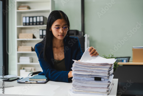 Asian businesswoman searching through pile of documents at desk