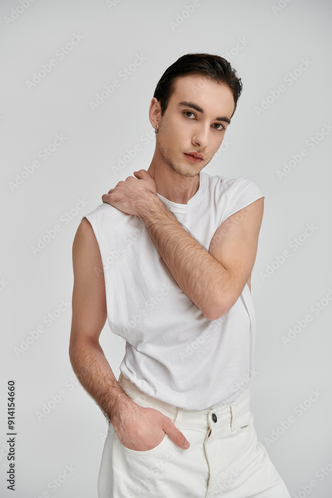 A man in a white sleeveless shirt and white jeans poses confidently against a plain white backdrop. A man in a white sleeveless shirt and white jeans poses confidently against a plain white backdrop.