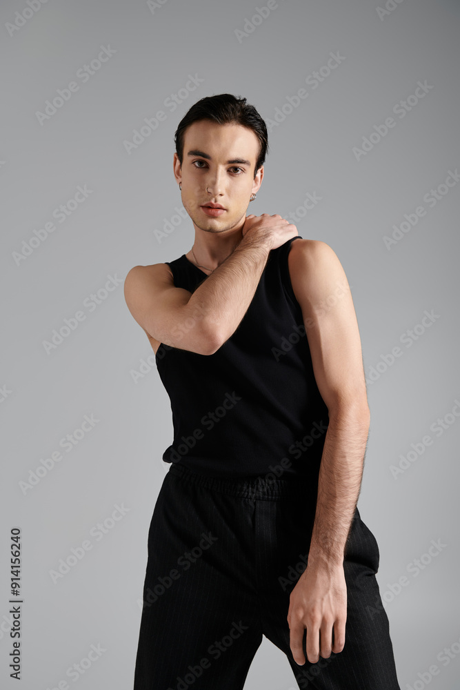 A confident man in black tank top against gray backdrop exudes style. A confident man in black tank top against gray backdrop exudes style.