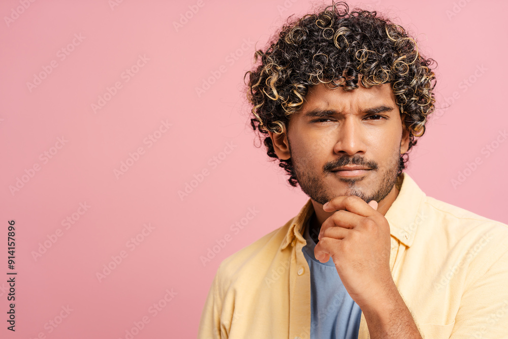Fototapeta premium Pensive young Indian adult man touching chin with hand on pink background