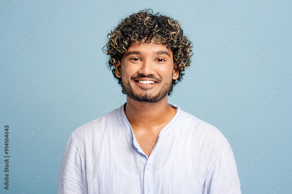 Young smiling Indian man with curly hair smiling on blue background Young smiling Indian man with curly hair smiling on blue background