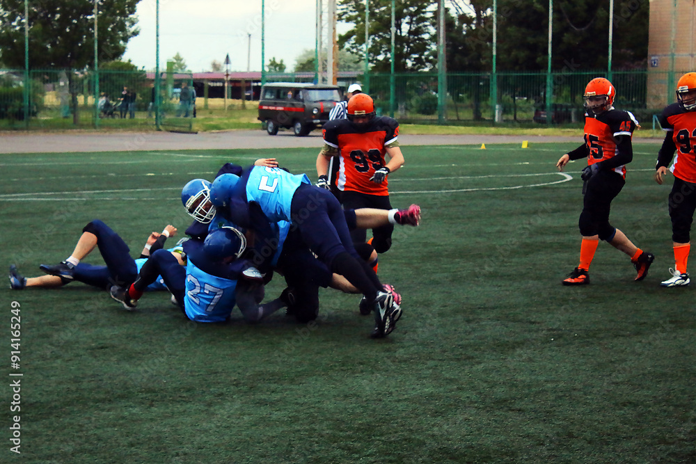 An American football player in a black and blue uniform leaned on a player in a black and orange uniform.
An American football player in a black and blue uniform leaned on a player in a black and orange uniform.