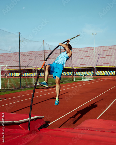 Фотография High jump practice in action, with focused and strong pole vaulter, competitive man in blue uniform training at outdoor stadium