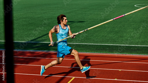 High jump practice session, with focused and strong young man, pole vaulter in blue uniform in motion, running with pole at outdoor stadium. Concept of sport, competition, tournament, active lifestyle