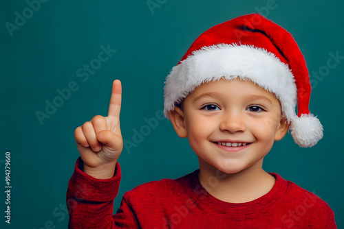 Happy young boy wearing a Santa's hat pointing with his finger, against a plain background