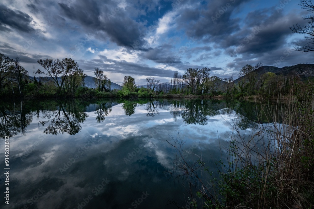 Serene landscape with a lake reflecting the cloudy sky and surrounding trees at dusk Serene landscape with a lake reflecting the cloudy sky and surrounding trees at dusk