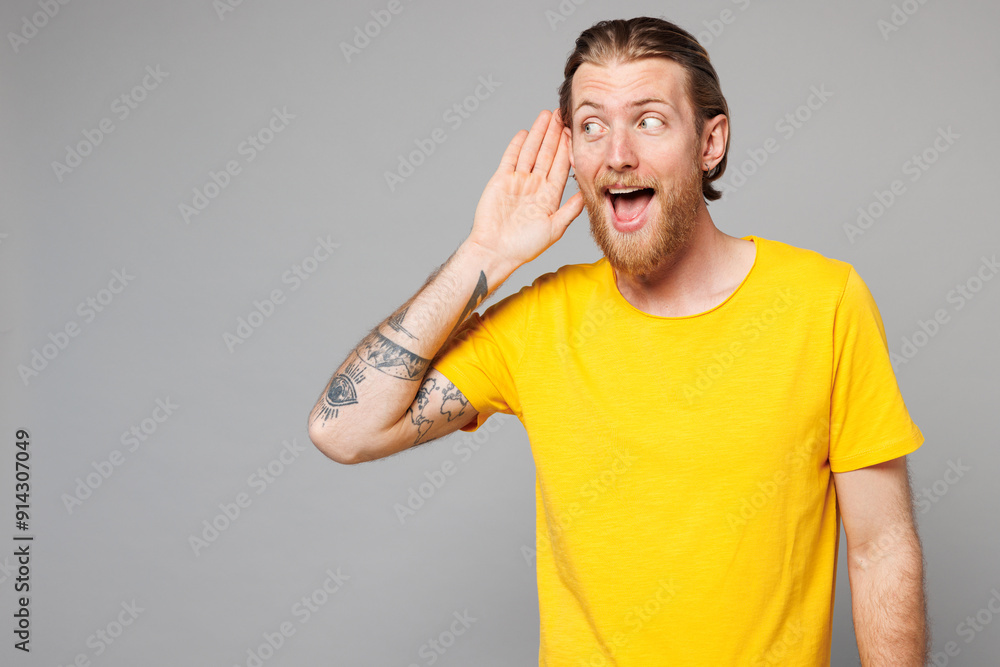 Young curious nosy Caucasian man he wearing yellow t-shirt casual clothes try to hear you overhear listening intently look aside isolated on plain grey background studio portrait. Lifestyle concept. Young curious nosy Caucasian man he wearing yellow t-shirt casual clothes try to hear you overhear listening intently look aside isolated on plain grey background studio portrait. Lifestyle concept.