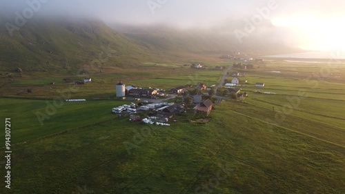 Farm buildings and fields under early morning mist and fog in Lofoten, Northern Norway by the Ryten mountain