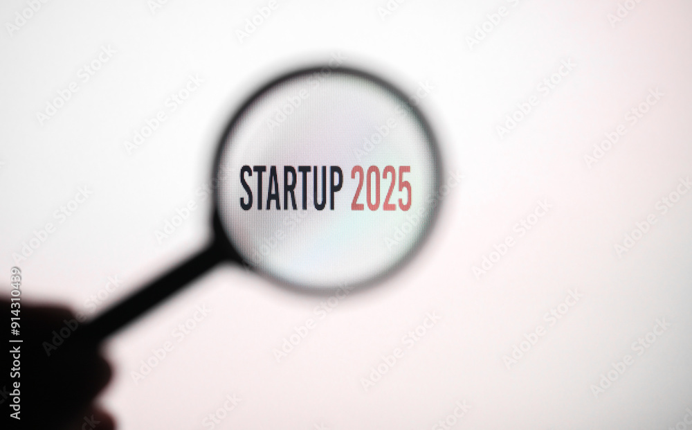 Phrase startup 2025 on white screen through a magnifying glass. Phrase startup 2025 on white screen through a magnifying glass.