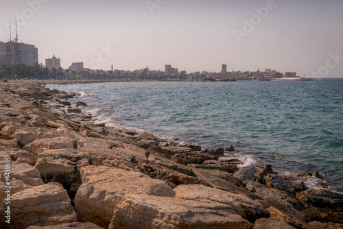 The empty coastline of the Tyre waterfront at the Mediterranean sea shore, with rocky beach, blue water and city view.
 photo