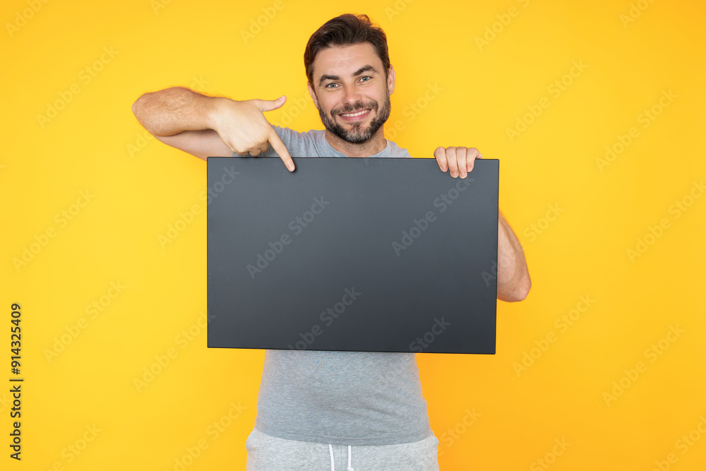 Happy man with blank banner isolated on studio background. Portrait of attractive man with empty blank poster. Man showing poster, pointing finger on signboard placard. Billboard or banner concept. Happy man with blank banner isolated on studio background. Portrait of attractive man with empty blank poster. Man showing poster, pointing finger on signboard placard. Billboard or banner concept.