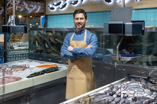 Photography Confident fishmonger standing with arms crossed in front of seafood display at fish market