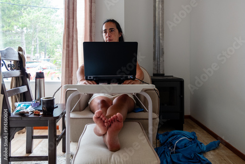 A woman is sitting on a footstool in front of a laptop photo