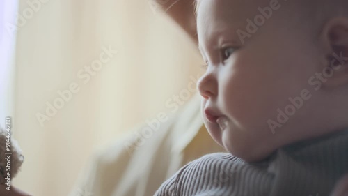 Extreme close-up of face of adorable Caucasian baby nestling in arms of unrecognizable young mother developing sensory skills by touching soft teddy bear photo