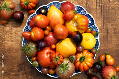 Obraz na płótnie Many garden tomatoes in different colors, shapes and varieties on a blue rustic plate on a wooden table. Tomatoe composition with space for text. w salonie
