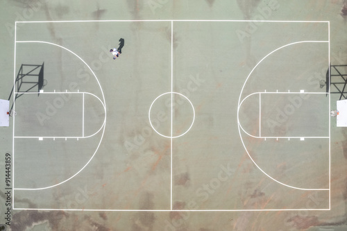 Direct overhead drone view of skateboarder on an empty basketball court on a sunny day