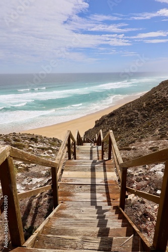 stairs leading down to a pristine beach with turquoise waves and a partly cloudy sky