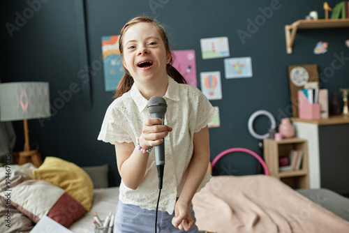 Young girl smiling and singing while holding microphone in colorful bedroom setting filled with artwork and cozy decor creating a cheerful atmosphere photo