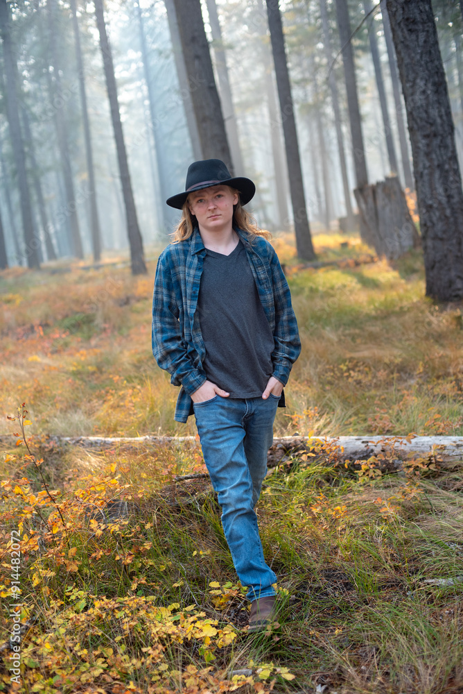 young man, wearing flannel shirt and jeans, walking though autumn forest