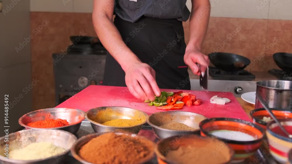 Chefs chop red and green bell peppers on a cutting board in front of bowls with spices, MSG seasonings and ingredients for dishes. Close-up. Chefs chop red and green bell peppers on a cutting board in front of bowls with spices, MSG seasonings and ingredients for dishes. Close-up.