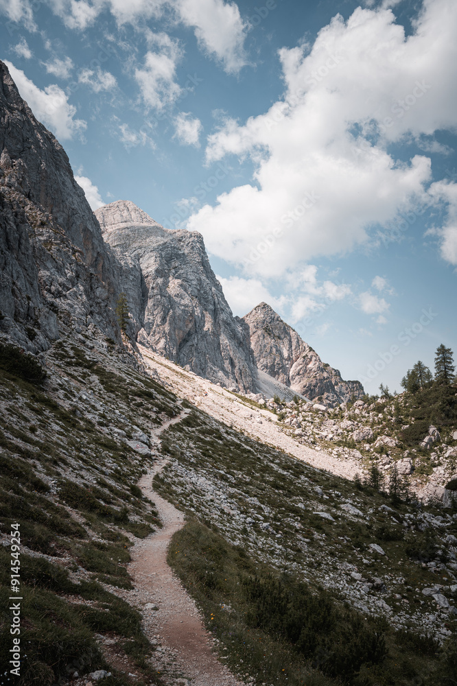Obraz premium Rocky mountain trail leading toward dramatic peaks and blue sky.