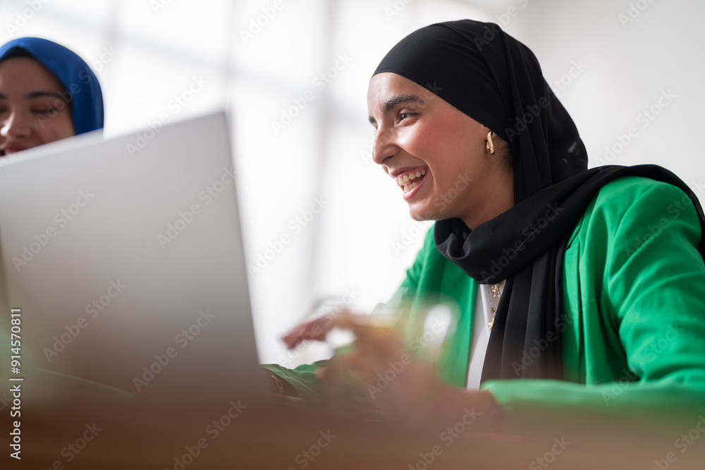 A woman in a black hijab and green blazer smiles as she works on her laptop in a bright office. Her positive demeanor adds to the professional yet friendly atmosphere of the workspace. A woman in a black hijab and green blazer smiles as she works on her laptop in a bright office. Her positive demeanor adds to the professional yet friendly atmosphere of the workspace.