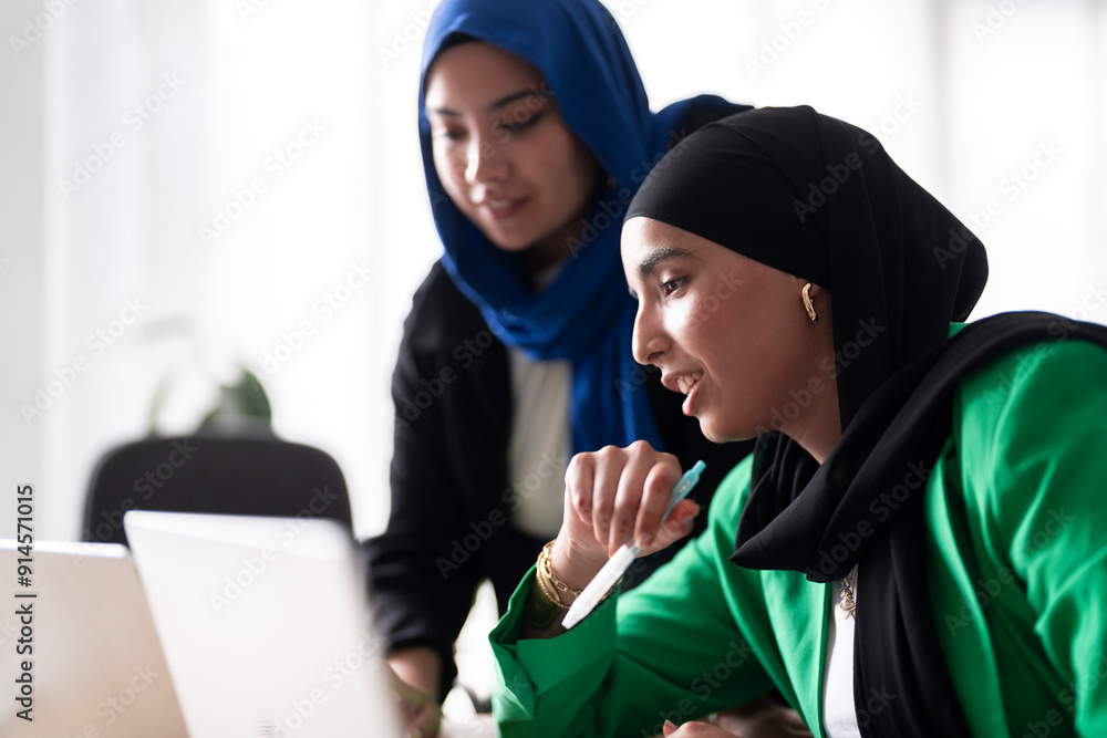 Two women in hijabs collaborate on a project while working on their ...