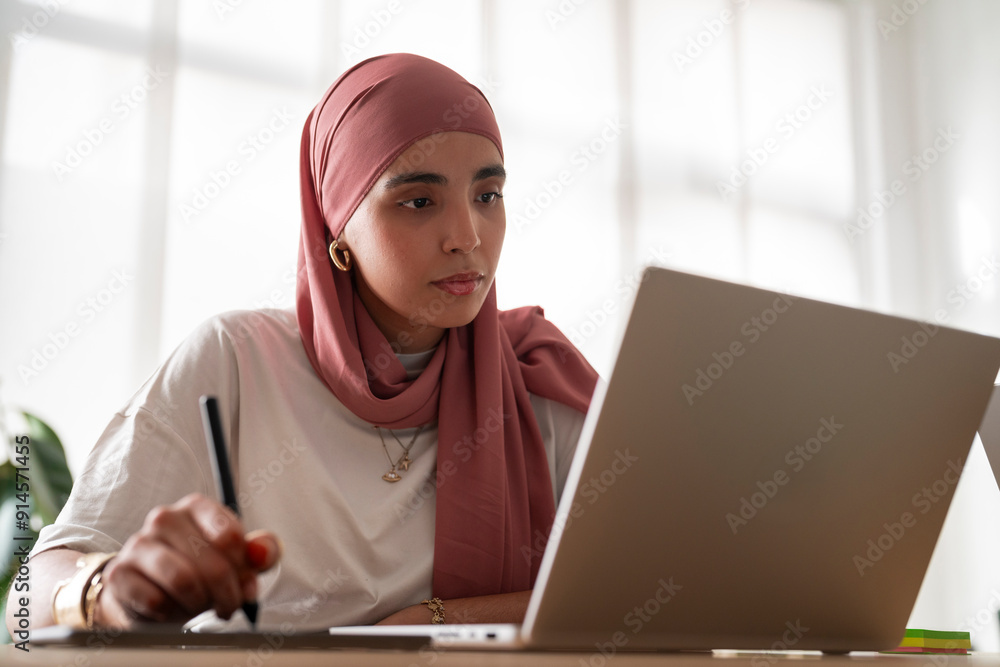 A woman in a dark red hijab works intently on her laptop, likely programming or designing for a 3D printing project. A woman in a dark red hijab works intently on her laptop, likely programming or designing for a 3D printing project.