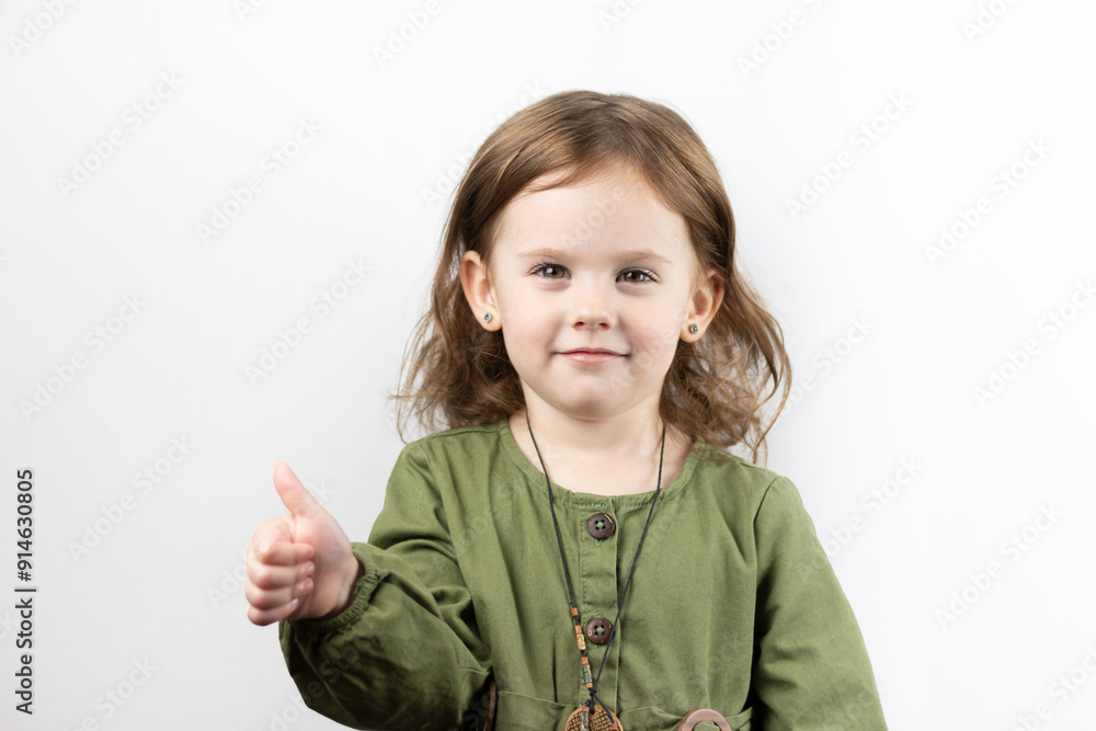 Little girl with blond hair in green dress with medallion making faces on white studio background. Little girl with blond hair in green dress with medallion making faces on white studio background.