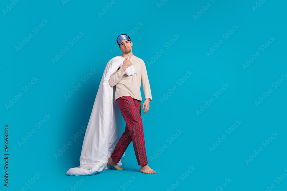 Full body photo of attractive young man hold blanket walking moody dressed pajama sleepover good night isolated on blue color background Full body photo of attractive young man hold blanket walking moody dressed pajama sleepover good night isolated on blue color background