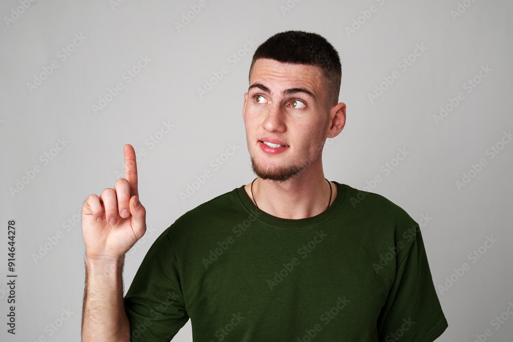 Young Man With Short Hair Wearing Green T-Shirt Pointing Upward Against Gray Background Young Man With Short Hair Wearing Green T-Shirt Pointing Upward Against Gray Background