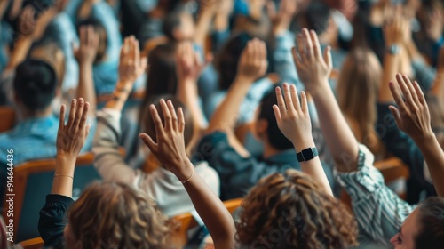 In a classroom environment, many individuals are raising their hands and arms, casting votes in a professional education context, with a focus on the indistinct audience.