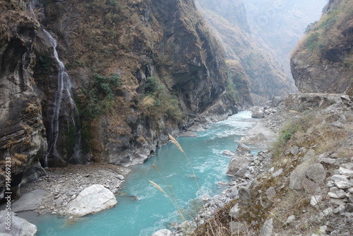 Turquoise river winds through a rugged valley in the nepalese himalayas, surrounded by towering mountains and lush greenery, creating a peaceful scene in a remote and wild landscape