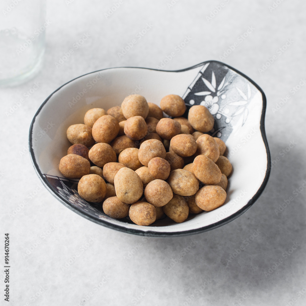 Fried coated peanuts in a white ceramic plate, cracker peanuts on a marble countertop, nigerian peanut snack in a small white plate Fried coated peanuts in a white ceramic plate, cracker peanuts on a marble countertop, nigerian peanut snack in a small white plate