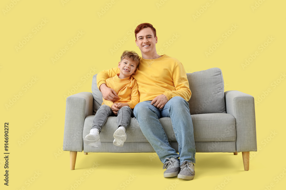 Little boy with his father hugging on sofa against yellow background Little boy with his father hugging on sofa against yellow background