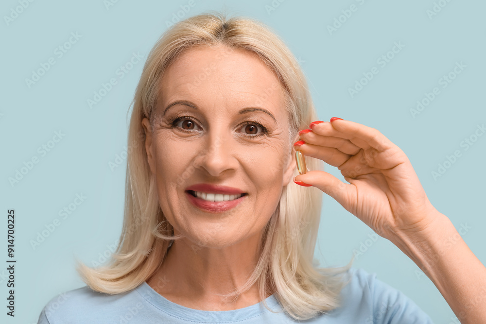 Mature woman with fish oil pill on light blue background Mature woman with fish oil pill on light blue background
