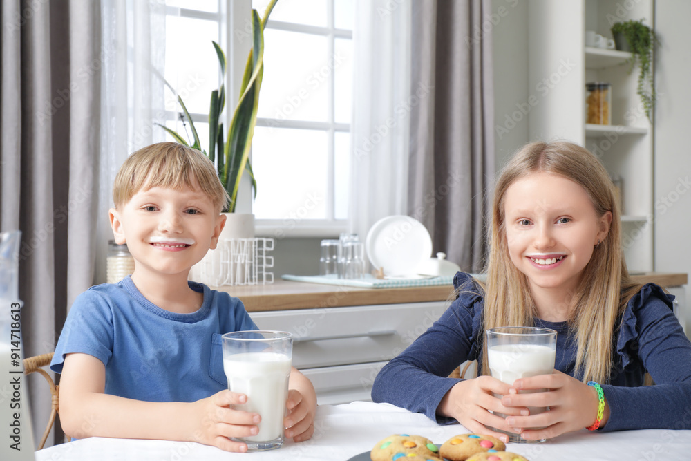 Happy children with glasses of milk at dining table in kitchen Happy children with glasses of milk at dining table in kitchen