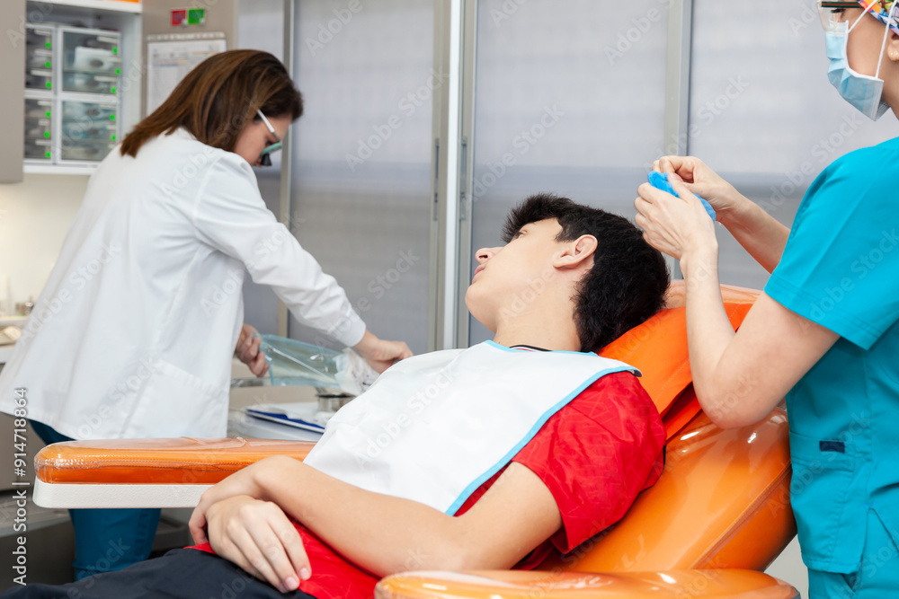 Obraz premium Young male patient being prepared for a skin lesion removal procedure. Dermatologist carrying out a removal of benign skin lesion on the face of a young male patient.