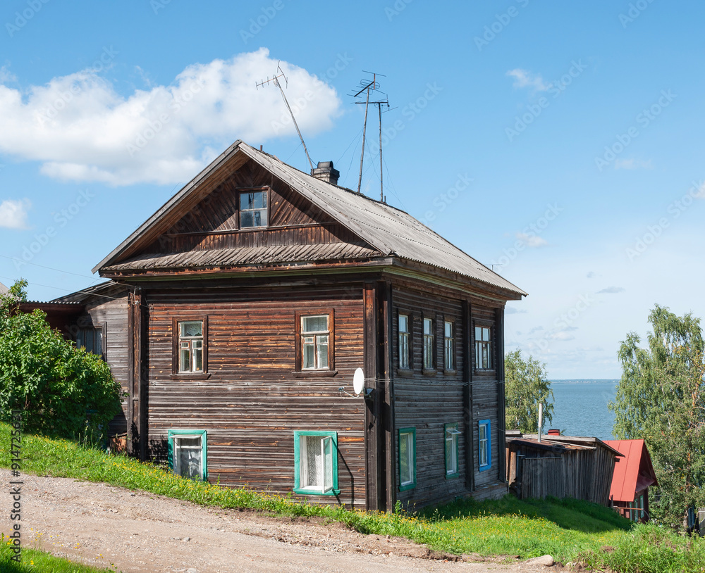 Old traditional two-storey wooden house on the shore of lake in Chukhloma town, Russia. Sunny summer day