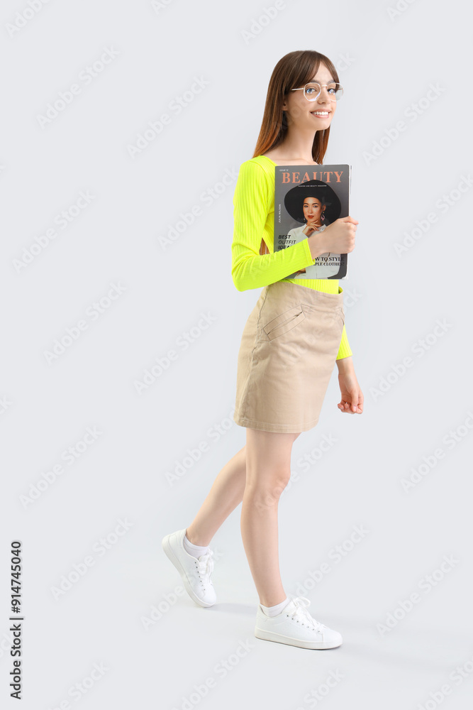 Young woman with magazine walking on light background Young woman with magazine walking on light background