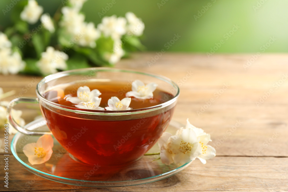 Hot jasmine tea in cup and flowers on wooden table, space for text Hot jasmine tea in cup and flowers on wooden table, space for text