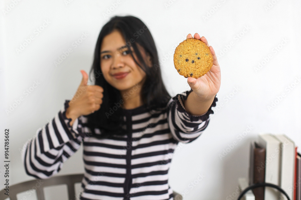 Friendly Young Asian Woman Giving Thumb Up While Holding Cookies At Home Friendly Young Asian Woman Giving Thumb Up While Holding Cookies At Home