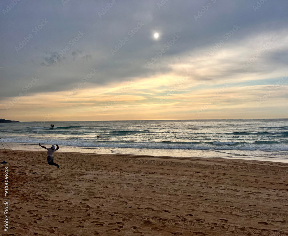 A volleyball player hitting a ball in the morning under the clouds on the beach